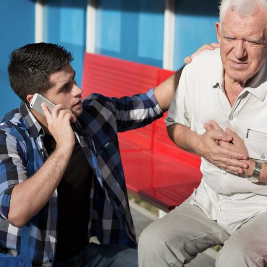 Erste-Hilfe-Situation: Ein junger Mann hilft einem Senior und wählt den Notruf