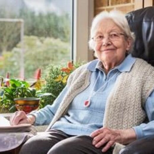 Wohnen im Alter: Eine Seniorin sitzt in einem Sessel und schaut freundlich in die Kamera