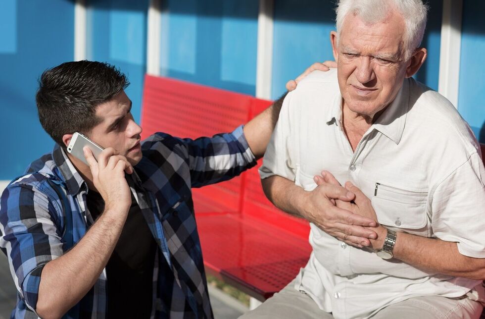 Erste-Hilfe-Situation: Ein junger Mann hilft einem Senior und wählt den Notruf