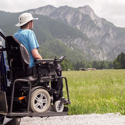 Rollstuhlfahrer vor Auto in den Bergen