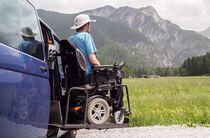 Rollstuhlfahrer vor Auto in den Bergen