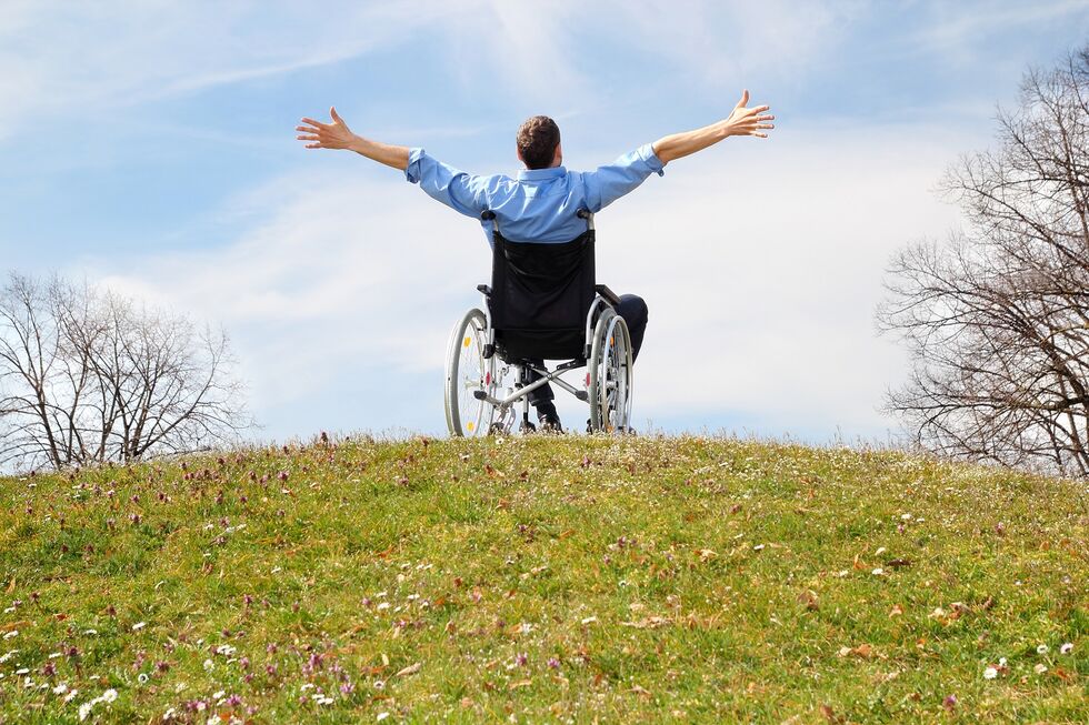 Rollstuhlfahrer sitzt im Garten und reißt begeistert die Arme in die Luft