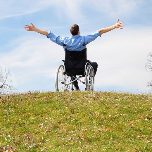 Rollstuhlfahrer sitzt im Garten und reißt begeistert die Arme in die Luft