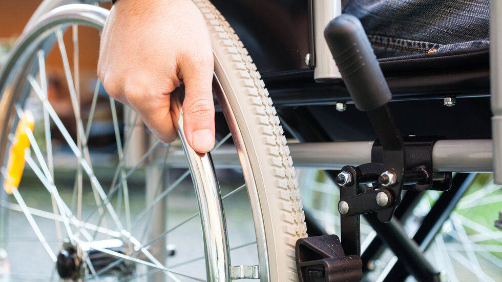 Eine Hand die das Rad vom Rollstuhl anschiebt