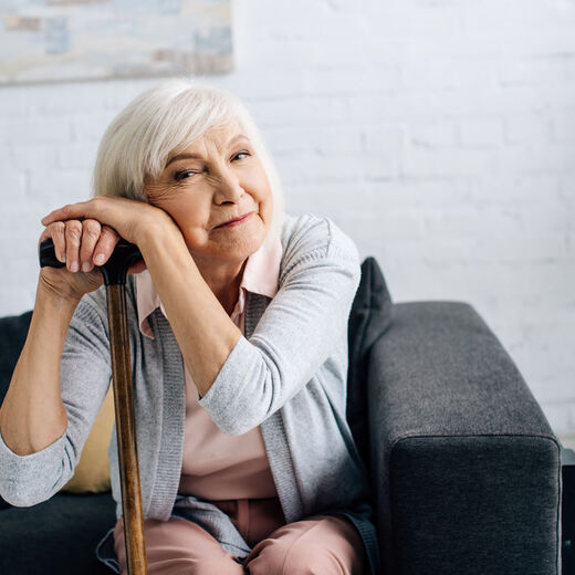 Selbstständig Leben im Alter: Eine Seniorin mit Stock in der Hand lächelt in die Kamera