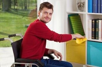 Rollstuhlfahrer putzt Regal in seiner Wohnung