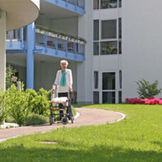 Seniorin geht mit ihrem Rollator durch den Garten eines Pflegeheims