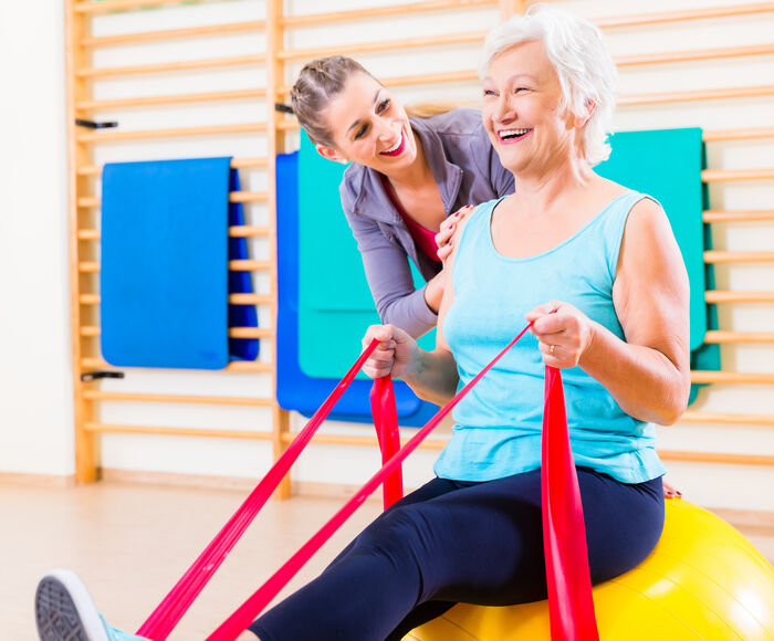 Eine macht Übungen mit einem Elastikband auf einem Gymnastikball 