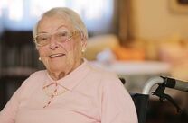Seniorin sitzt lächelnd im Rollstuhl
