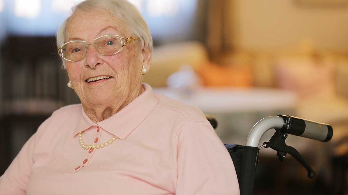 Seniorin sitzt lächelnd im Rollstuhl