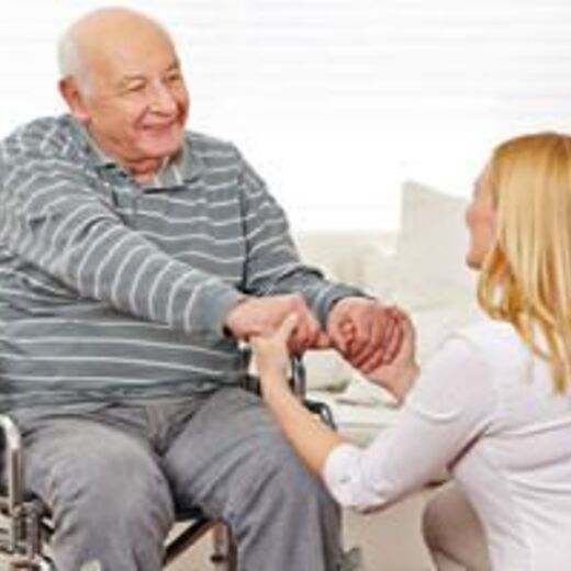 Pflegerin hält die Hände von Senior im Rollstuhl