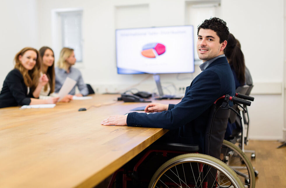Rollstuhlfahrer in Meeting am geförderten barrierefreien Arbeitsplatz