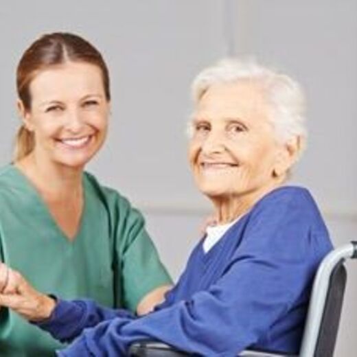 Pflegepersonal hält die Hand von einer alten Dame im Rollstuhl