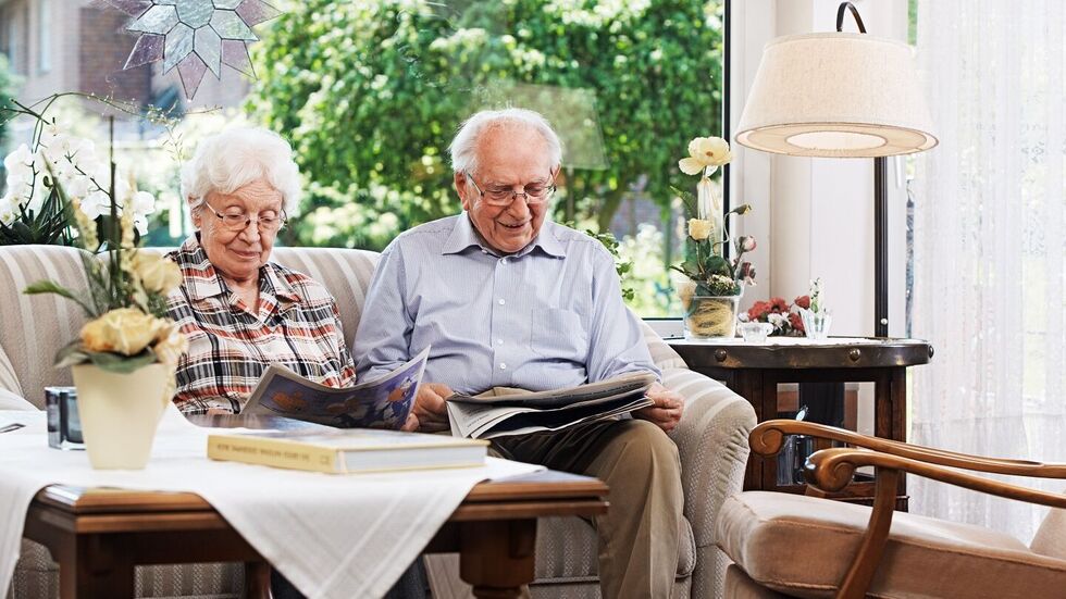 Älteres Paar sitzt auf dem Sofa und liest Zeitung
