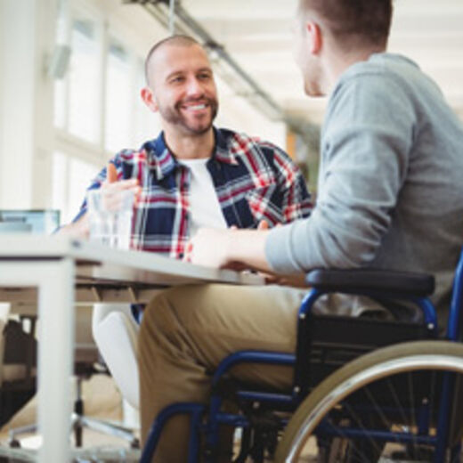 Inklusion in der Praxis: Ein Rollstuhlfahrer unterhält sich mit einem Kollegen am Arbeitsplatz