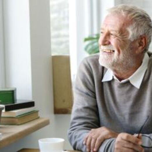 Älterer Mann schaut lächelnd aus dem Fenster und sitzt am Tisch