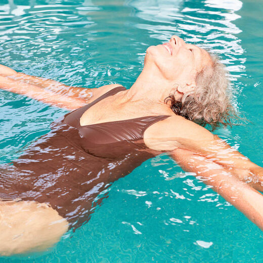 Seniorin beim Rückenschwimmen mit Schwimmnudel.