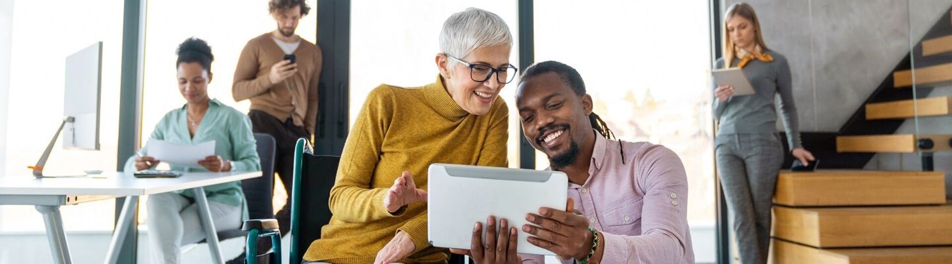 Inklusion am Arbeitsplatz in der Praxis Junger Mann zeigt seiner Kollegin im Rollstuhl etwas auf dem Tablet