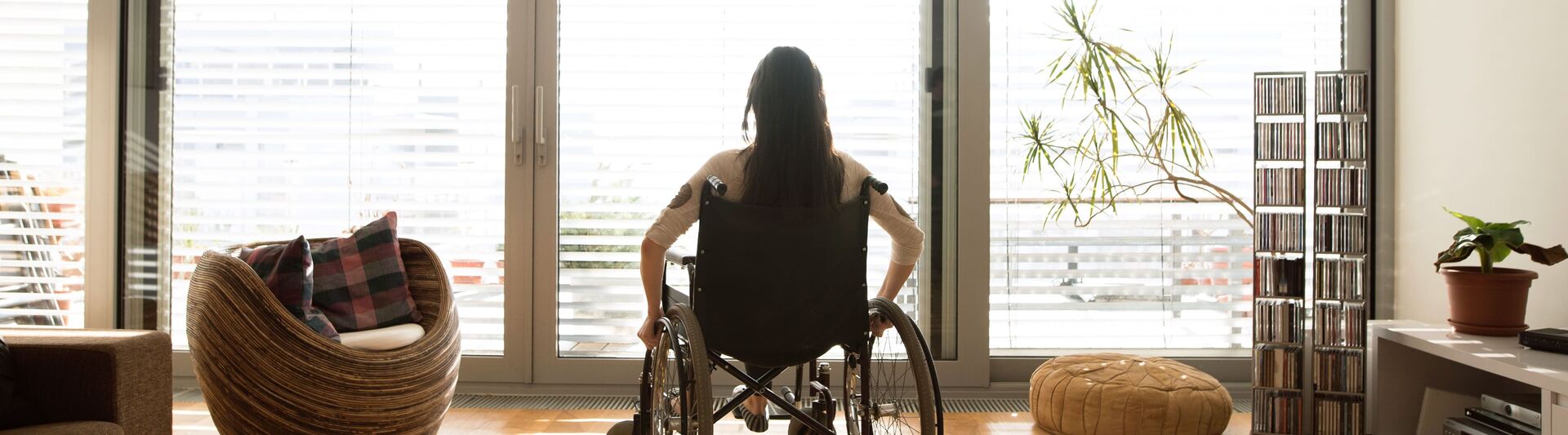 Wohnen mit Behinderung: Eine Frau im Rollstuhl schaut aus dem Fenster in ihrem Wohnzimmer