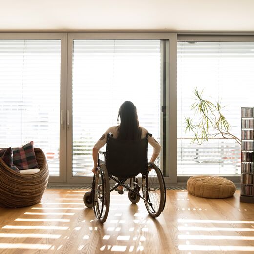 Wohnen mit Behinderung: Eine Frau im Rollstuhl schaut aus dem Fenster in ihrem Wohnzimmer