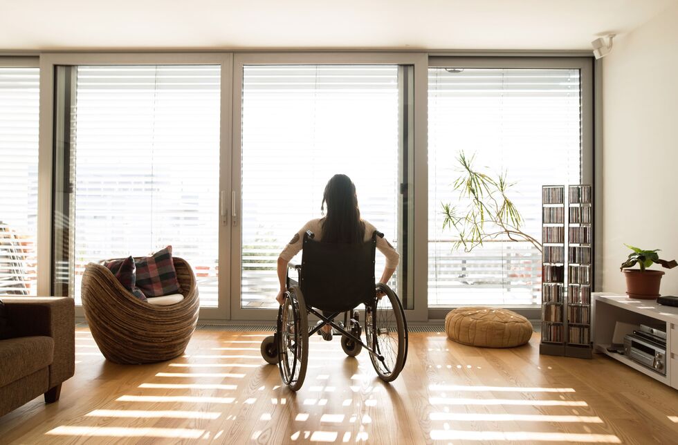 Wohnen mit Behinderung: Eine Frau im Rollstuhl schaut aus dem Fenster in ihrem Wohnzimmer