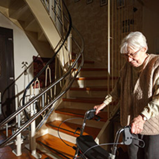 Treppen überwinden mit einem Stehlift: Eine Seniorin mit Rollator vor einer Treppe