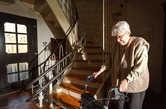 Treppen überwinden mit einem Stehlift: Eine Seniorin mit Rollator vor einer Treppe