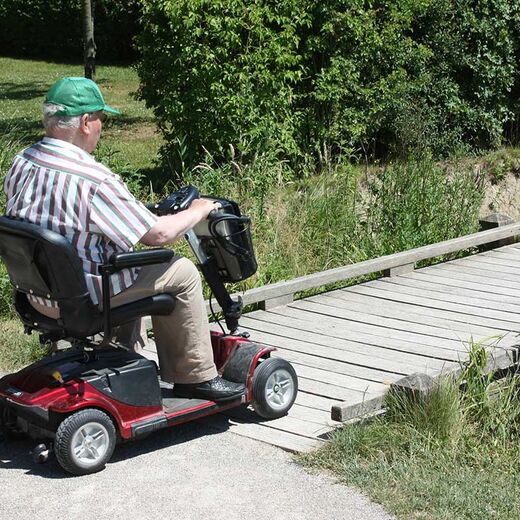 Senior im Elektromobil fährt über eine Brücke