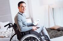 Leben mit Behinderung: Ein junger Mann im Rollstuhl hält ein Tablet in der Hand