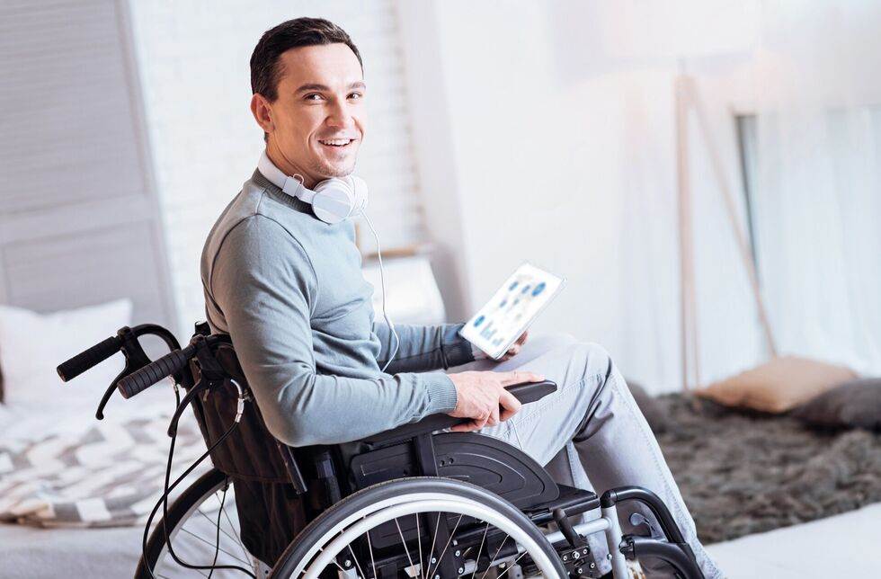 Leben mit Behinderung: Ein junger Mann im Rollstuhl hält ein Tablet in der Hand