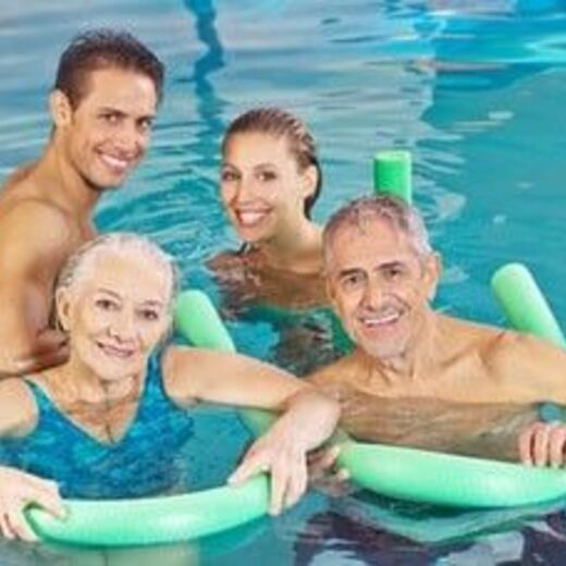Vier Senioren stehen lächelnd mit Schwimmnudel im Wasser