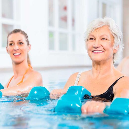 Eine Rentnerin und eine junge Frau nehmen gemeinsam an einem Wassergymnastik-Kurs teil