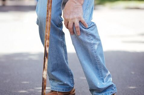 Knieschmerzen beim Treppensteigen: Eine Person hält sich beim Gehen mit Stock das Knie