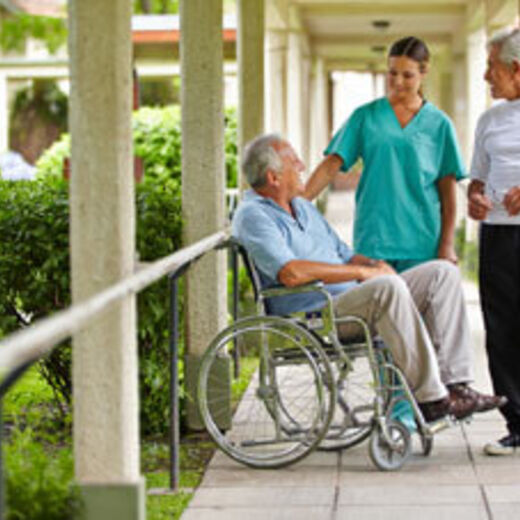 Eine Pflegerin steht im Garten mit einem Rollstuhlfahrer und einem älteren Herrn