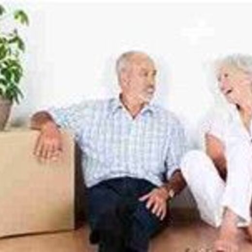 Älteres Ehepaar lächelt sich an und sitzt dabei neben Umzugkartons