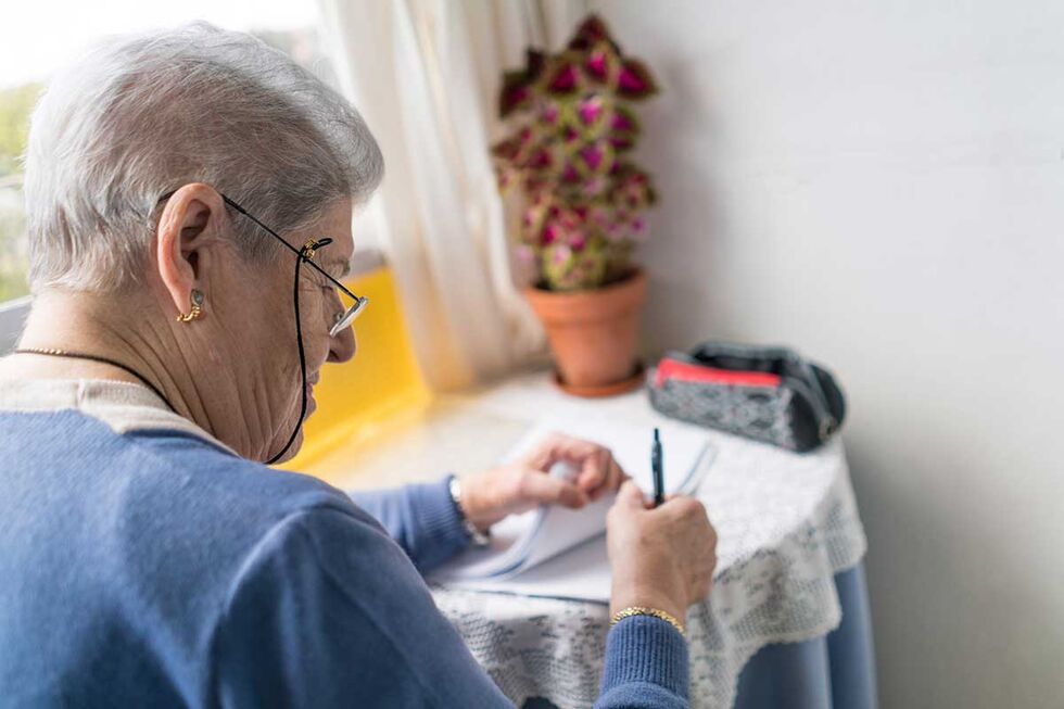 Rote Schleife Seniorin schaut in den Ferne mit einer roten Schleife an der Hand