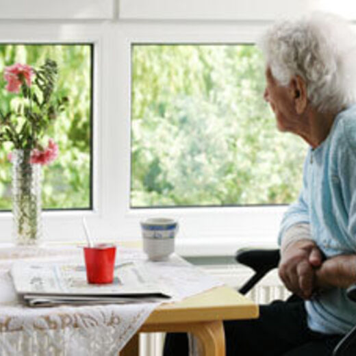 Eine Seniorin sitzt am Tisch und schaut aus dem Fenster