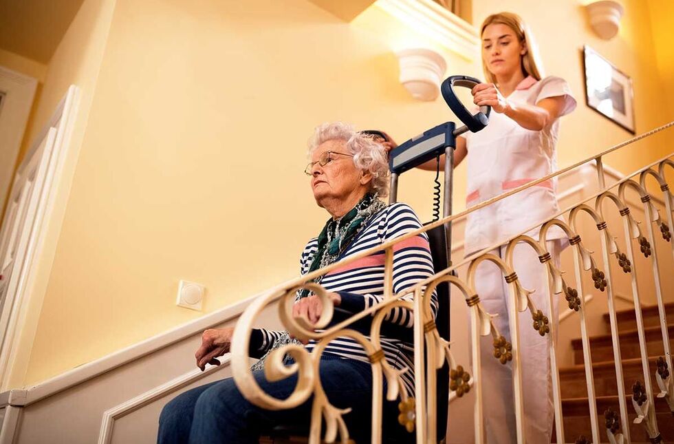 Eine Pflegerin hilft einer Seniorin in einem Lift