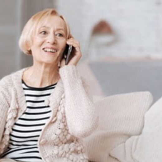 Seniorin telefoniert mit Smartphone während sie auf der Couch sitzt