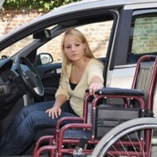 Rollstuhlfahrerin sitzt im Auto und klappt ihren Rollstuhl zusammen