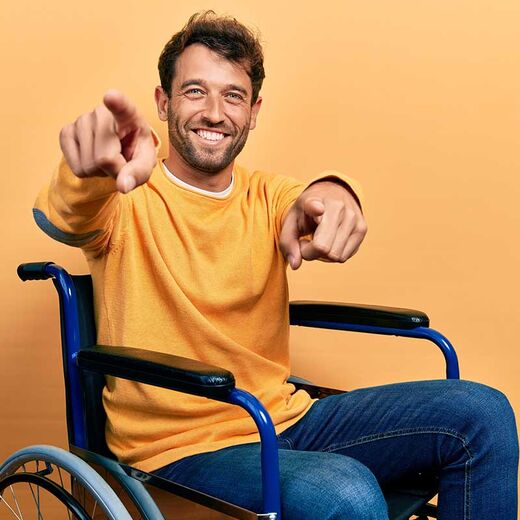 Mann im Rollstuhl lächelt und zeigt Richtung Kamera