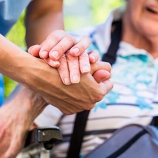 Pfleger und Seniorin halten sich die Hände
