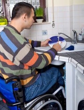 Unterfahrbare Spüle in einer barrierefreien Küche Rollstuhlfahrer sitzt vor einer unterfahrbaren Spüle