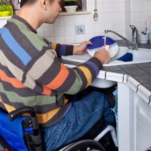 Mann im Rollstuhl wäscht Geschirr in barrierefreier Küche ab