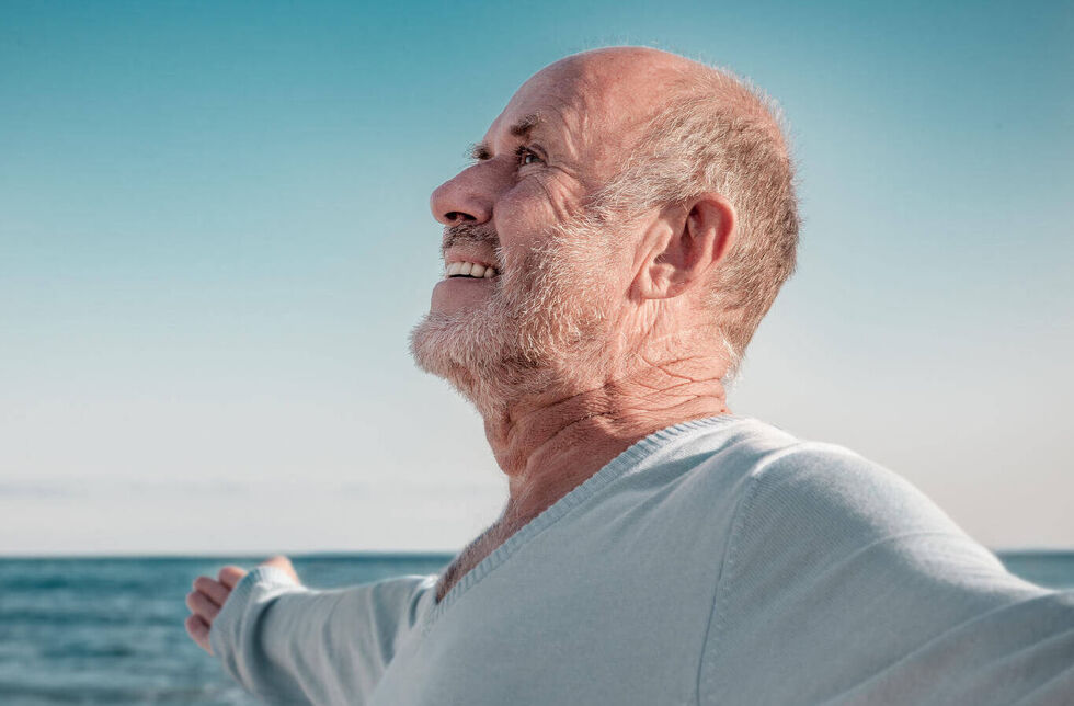 Senior atmet am Strand frische Meeresluft ein. 