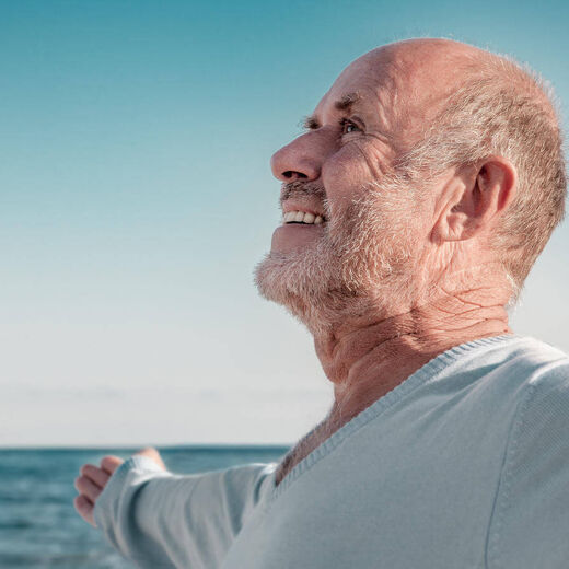 Senior am Meer weitet die Arme und lächelt in den Himmel