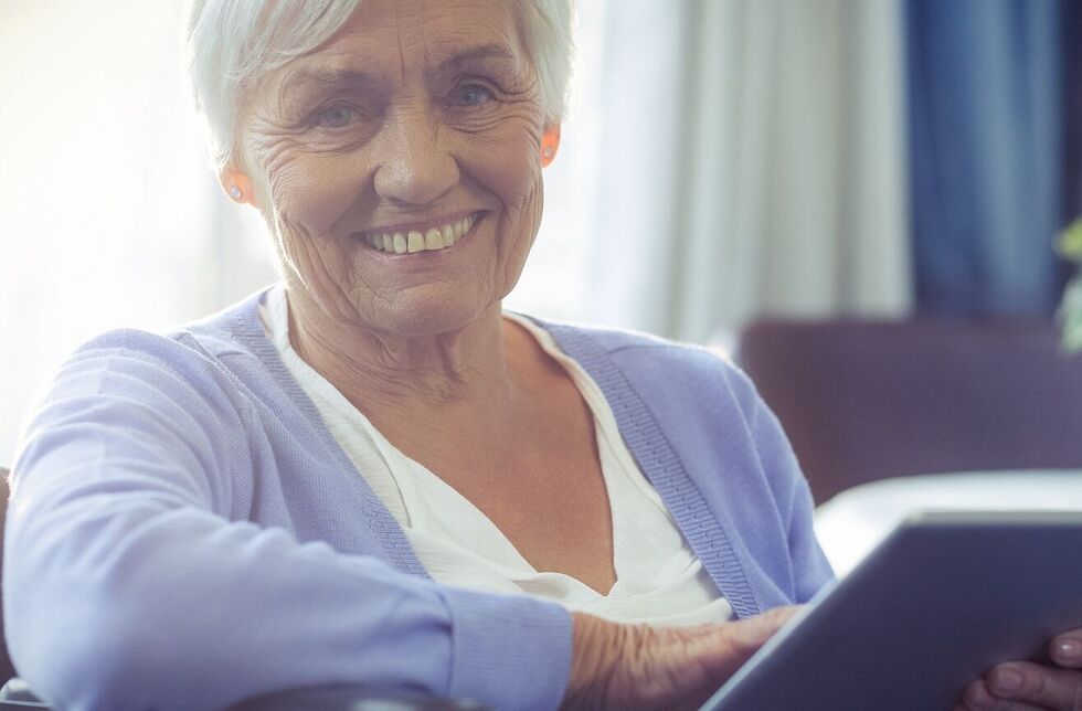 Ältere Frau im Rollstuhl mit Tablet in der Hand
