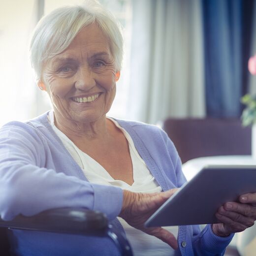 Ältere Frau im Rollstuhl mit Tablet in der Hand