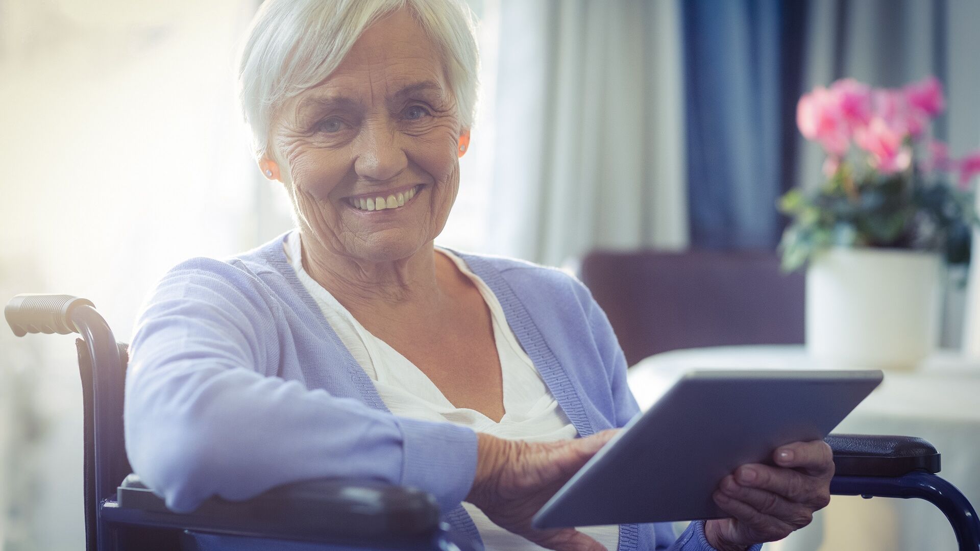 Ältere Frau im Rollstuhl mit Tablet in der Hand