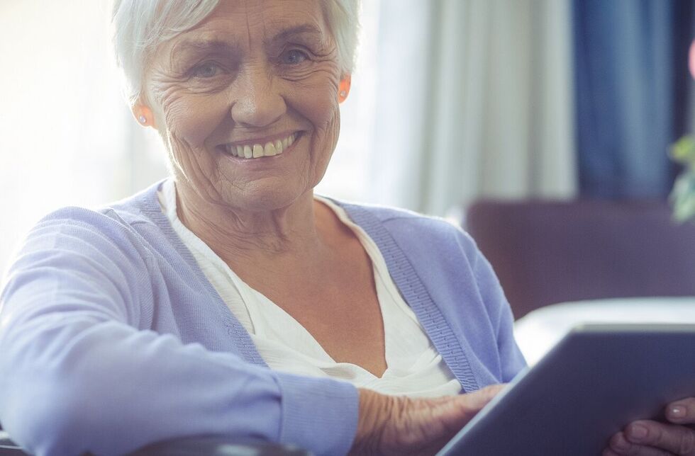 Ältere Frau im Rollstuhl mit Tablet in der Hand